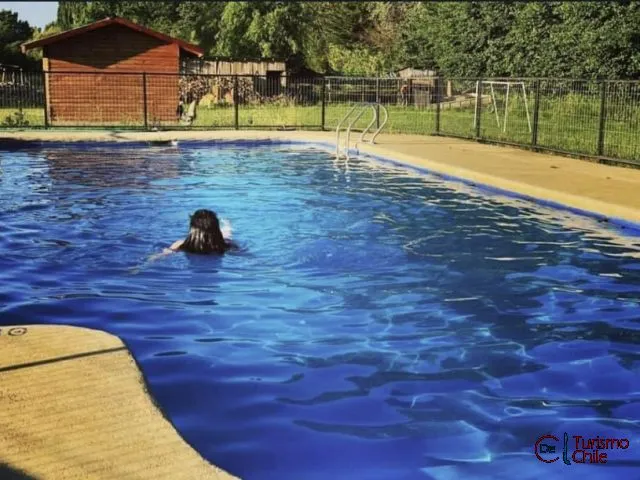 Persona nadando en la piscina de Cabañas Mi Casa con juegos de niños al fondo