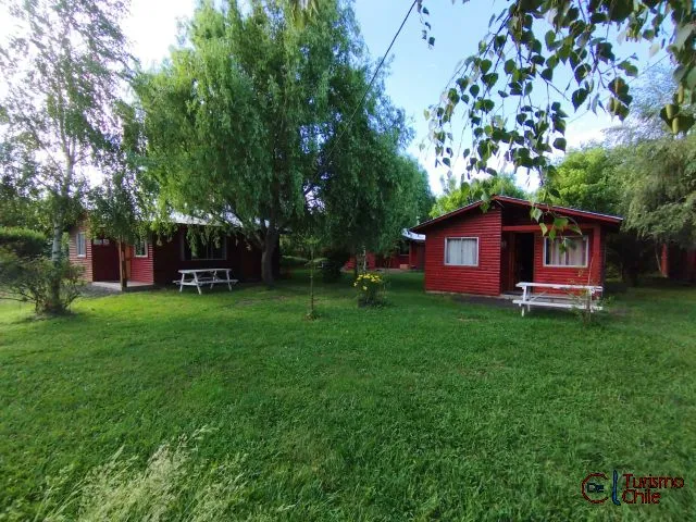 Cabañas rojas de madera rodeadas de jardín y árboles en Cabañas Mi Casa, Saltos del Laja